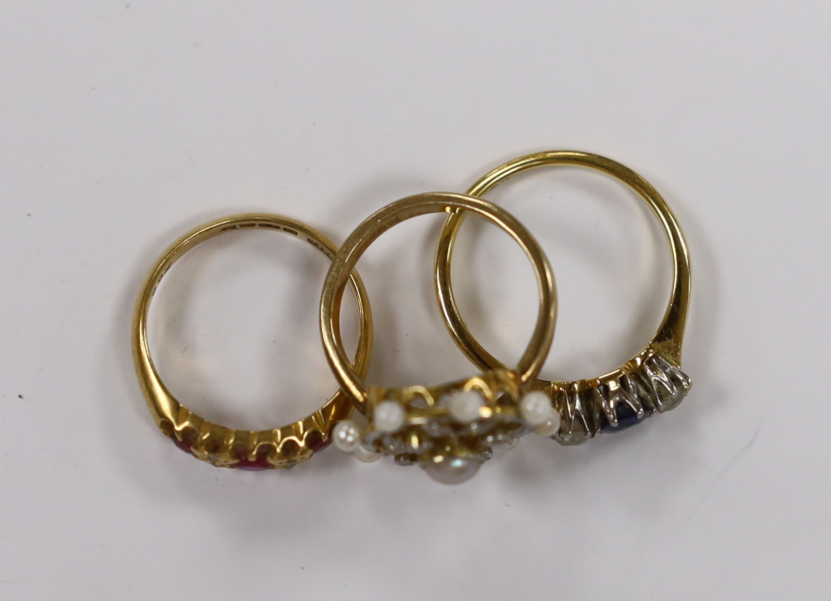 An 18ct, sapphire and diamond set three stone ring, a George V 18ct gold and three red stone set ring with diamond chip spacers and a yellow metal seed pearl and diamond chip set cluster ring (pearl missing), gross weigh